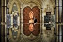 An artist and his huge beechwood sculpture titled 'St Joan of Arc'is reflected in Salisbury Cathedral font