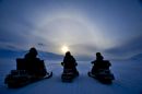 People on ski-doo's admire a halo, also known as a nimbus, icebow or Gloriole, which is an optical phenomenon produced by ice crystals and is produced by ice crystals in cirrus clouds high in the upper troposphere, on the island of Spitsbergen on the Svalbard archipelago in the Arctic circle as the Norwegian islands enter summer 'midnight sun' season