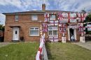 An avid England football fan chills out on his front doorstep at his semi-detached house in the Knowle West area of Bristol where he has adorned it with England flags