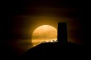 Revellers watch a huge red moon rise above Glastonbury Tor in Somerset, UK as the Earth's sattelite is its closest for years, producing a 'supermoon'