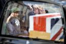 A young man salutes and pays his respects as a hearse passes by on the High Street