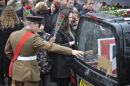 A serving soldier reaches for the back of the hearse as it pulls away on the High Street