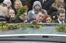 A man touches the top of a hearse as people lay flowers